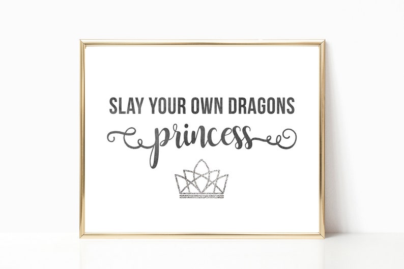 May include: A framed print with the text "SLAY YOUR OWN DRAGONS princess" in black script with a silver glitter crown underneath.