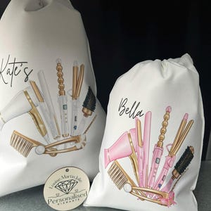 Pode incluir: Duas bolsas de lona brancas com cord&atilde;o de ajuste, personalizadas com os nomes "Kate's" e "Bella". Cada bolsa apresenta uma ilustra&ccedil;&atilde;o colorida de ferramentas para pentear o cabelo, incluindo um secador de cabelo, um modelador de cachos, uma prancha e escovas. As bolsas s&atilde;o perfeitas para guardar e organizar as ferramentas para pentear o cabelo.