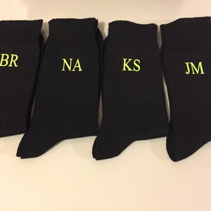 May include: Four black socks with white embroidered initials: BR, NA, KS, and JM.