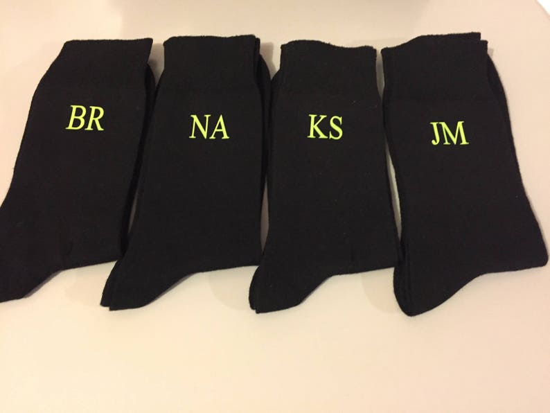 May include: Four black socks with white embroidered initials: BR, NA, KS, and JM.