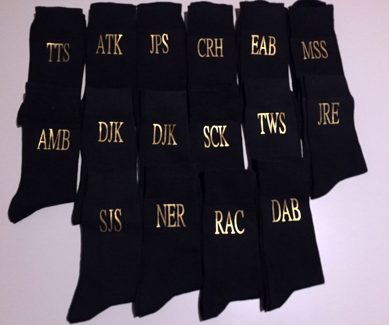 May include: A collection of black socks with gold embroidered initials. The initials include TTS, ATK, JPS, CRH, EAB, MSS, AMB, DJK, SCK, TWS, JRE, SIS, NER, RAC, and DAB.
