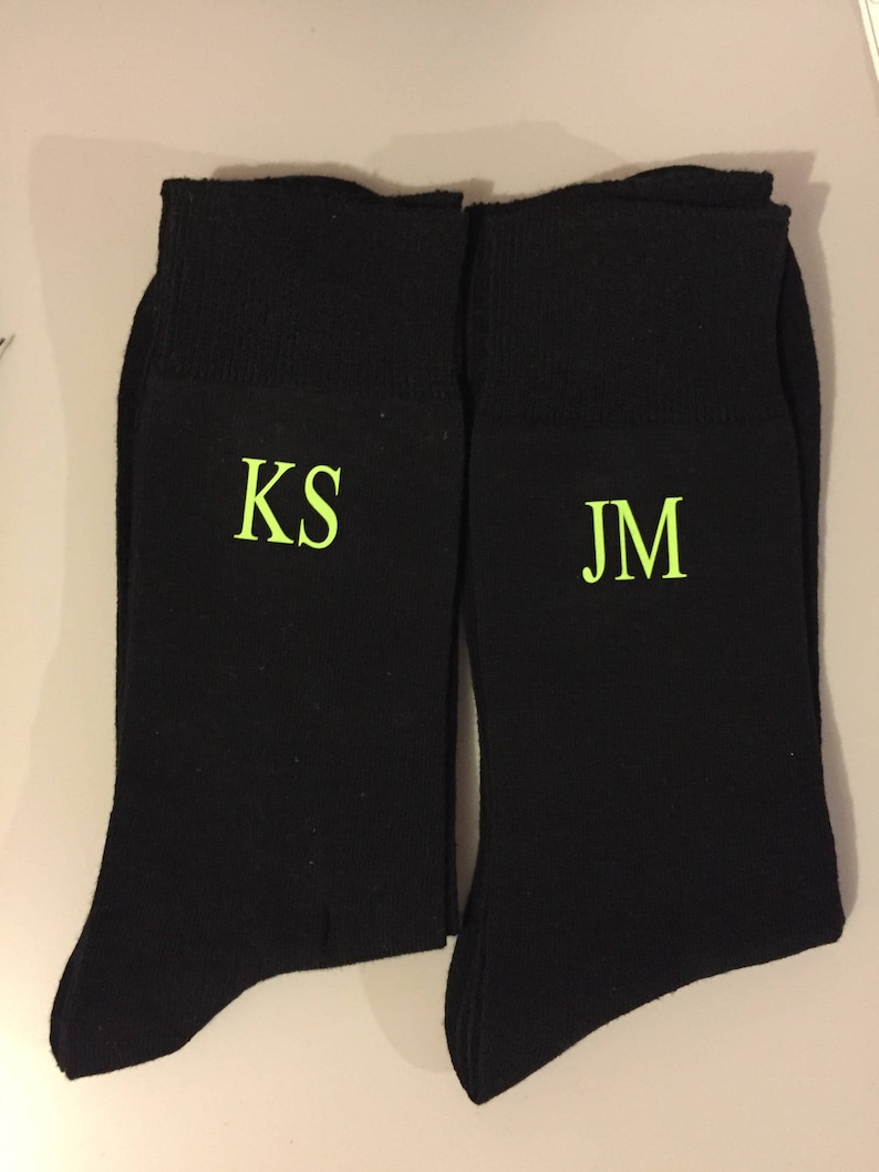 May include: Two pairs of black socks with the initials "KS" and "JM" embroidered in green on the front.