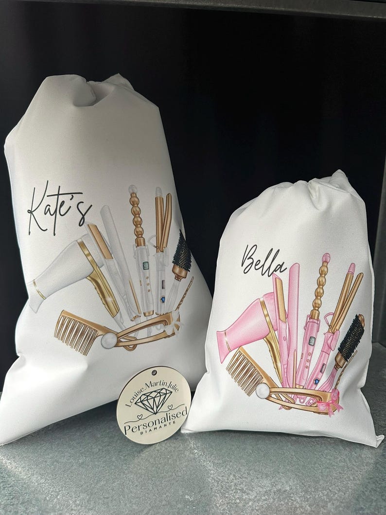 Pode incluir: Duas bolsas brancas de cord&atilde;o com os nomes personalizados "Kate's" e "Bella" impressos nelas. As bolsas apresentam ilustra&ccedil;&otilde;es de ferramentas para pentear o cabelo, como um secador de cabelo, um modelador de cachos e um pente. Uma pequena etiqueta de madeira com o texto "Louise Martin Julie Personalised Diamante" &eacute; vis&iacute;vel no canto inferior esquerdo.