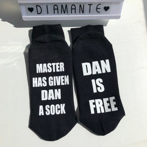 May include: A pair of black socks with white text. One sock says "Master has given Dan a sock" and the other sock says "Dan is free".