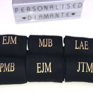 May include: Six pairs of black socks with gold embroidered initials. The initials are EJM, MJB, LAE, PMB, EJM, and JTM.