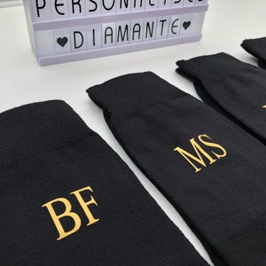 May include: Four black socks with gold embroidered initials: BF, MS, RZ. The socks are folded and arranged in a row.