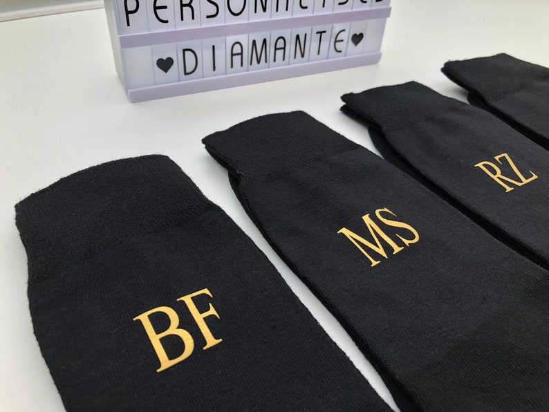 May include: Four black socks with gold embroidered initials: BF, MS, RZ. The socks are folded and arranged in a row.