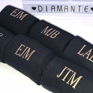 May include: Six black fabric wrist cuffs with gold embroidered initials. The initials are EJM, PMB, MJB, LAE, and JTM.