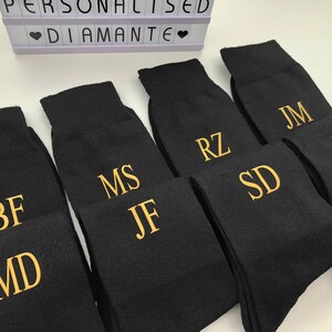 May include: Six pairs of black socks with gold embroidered initials. The initials are BF, MD, MS, JF, RZ, SD, JM, and JB.