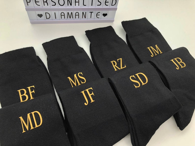 May include: Six pairs of black socks with gold embroidered initials. The initials are BF, MD, MS, JF, RZ, SD, JM, and JB.