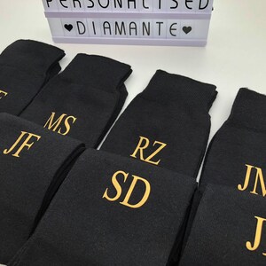 May include: A set of eight black socks with gold embroidered initials. The initials are: RF, JF, MS, RZ, SD, JM, and JB.
