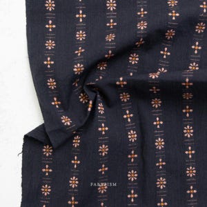 May include: Dark navy fabric with a repeating pattern of vertical stripes. Each stripe features small, stylized floral and cross-like designs in peach and gold. The word "FABRISM" is visible in the lower right corner.