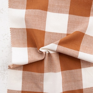May include: A close-up of a brown and white gingham fabric. The fabric is folded and has a soft, textured look.
