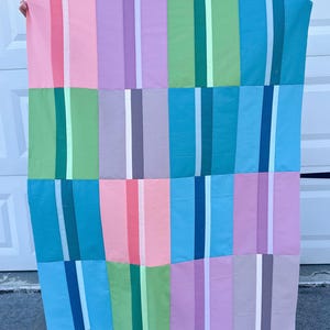 May include: A quilt with a patchwork design featuring alternating stripes of pink, purple, green, and blue.