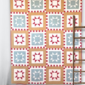 May include: A large, handmade quilt with a repeating star pattern. The quilt features alternating squares of red and white stars on a light blue background, framed by red and white borders. The quilt is displayed against a white wall.
