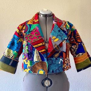 Puede incluir: Una chaqueta corta de patchwork colorida. La chaqueta está hecha de diferentes telas con varios patrones y colores, incluyendo rojo, azul, verde, amarillo y naranja.