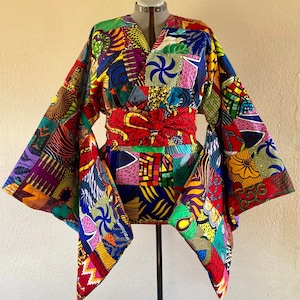 May include: A colorful kimono-style top with a patchwork design featuring various geometric shapes and floral patterns in shades of red, yellow, green, blue, and purple. The top has a V-neckline and a wide, flowing sleeve.