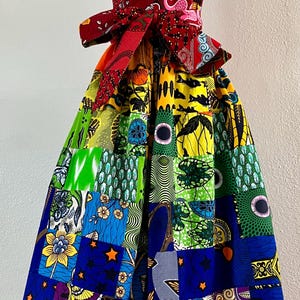 Puede incluir: Vestido patchwork sin tirantes con una vibrante mezcla de colores y estampados. El corpiño es rojo con estampado de flamencos, y la falda presenta un diseño patchwork con varios motivos geométricos y florales. Un gran lazo acentúa la cintura.