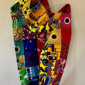 Puede incluir: Un colorido patchwork de tela con una variedad de patrones y colores, incluyendo rojo, amarillo, verde, azul y negro. La tela está dispuesta en un patrón geométrico y está doblada de una manera que crea una forma única.