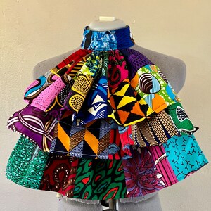 May include: A colourful fabric collar with multiple layers of different patterned fabrics in shades of pink, blue, green, yellow, orange, and black.