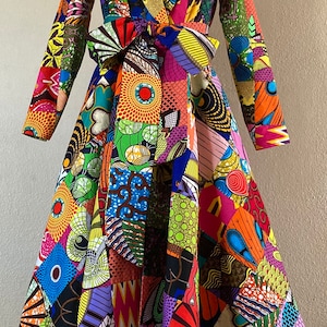 Puede incluir: Un vestido de manga larga con un diseño de patchwork colorido. El vestido tiene un escote en V, un corpiño ajustado y una falda completa. La tela es una mezcla de colores brillantes y patrones, incluyendo rojo, naranja, amarillo, verde, azul y morado.