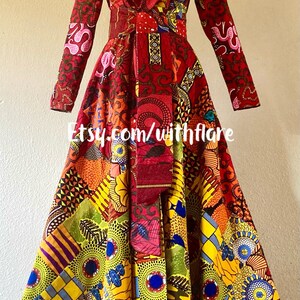 May include: A long-sleeved red dress with a colorful patterned fabric. The dress has a wrap-style bodice and a flared skirt. The fabric features a variety of geometric and floral designs in shades of red, yellow, blue, green, and pink. The dress is tied at the waist with a red sash. The text "Etsy.com/withflare" is visible on the dress.