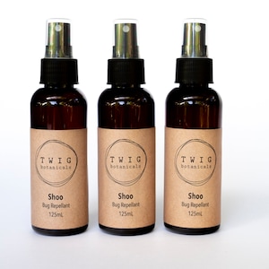 Puede incluir: Tres botellas de vidrio marr&oacute;n con pulverizador de "Shoo Bug Repellant" con tapas negras y etiquetas color canela. Cada etiqueta tiene el texto "TWIG botanicals" y "125ml". Las botellas est&aacute;n dispuestas en fila sobre un fondo blanco.