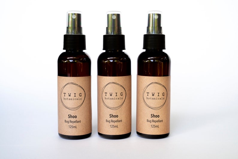 Puede incluir: Tres botellas de vidrio marr&oacute;n con pulverizador de "Shoo Bug Repellant" con tapas negras y etiquetas color canela. Cada etiqueta tiene el texto "TWIG botanicals" y "125ml". Las botellas est&aacute;n dispuestas en fila sobre un fondo blanco.