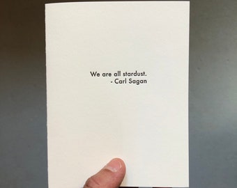 May include: A white card with the quote "We are all stardust. - Carl Sagan" printed in black.