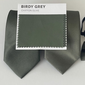 May include: Olive green neckties with varying textures are displayed, alongside a fabric swatch labeled "Birdy Grey Chiffon Olive." The ties showcase different patterns, including a ribbed design and a textured weave, suggesting options for formal wear.