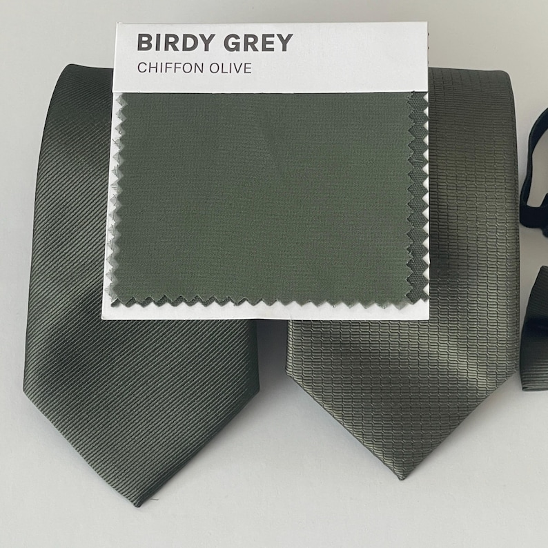 May include: Olive green neckties with varying textures are displayed, alongside a fabric swatch labeled "Birdy Grey Chiffon Olive." The ties showcase different patterns, including a ribbed design and a textured weave, suggesting options for formal wear.