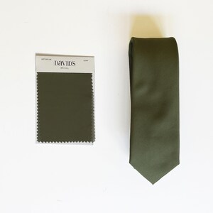 May include: Olive green necktie with a diagonal weave pattern, next to a fabric swatch. The swatch is labeled "MRTNGOLIVE" and "DAVID'S BRIDAL". The tie is a classic style, suitable for formal occasions.