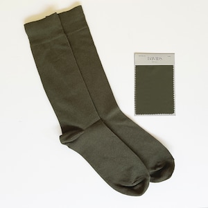 May include: A pair of olive green socks with a matching fabric swatch from David's Bridal. The socks are knee-high and made of a smooth material. The swatch is labeled "Chiffon" and is a solid color.