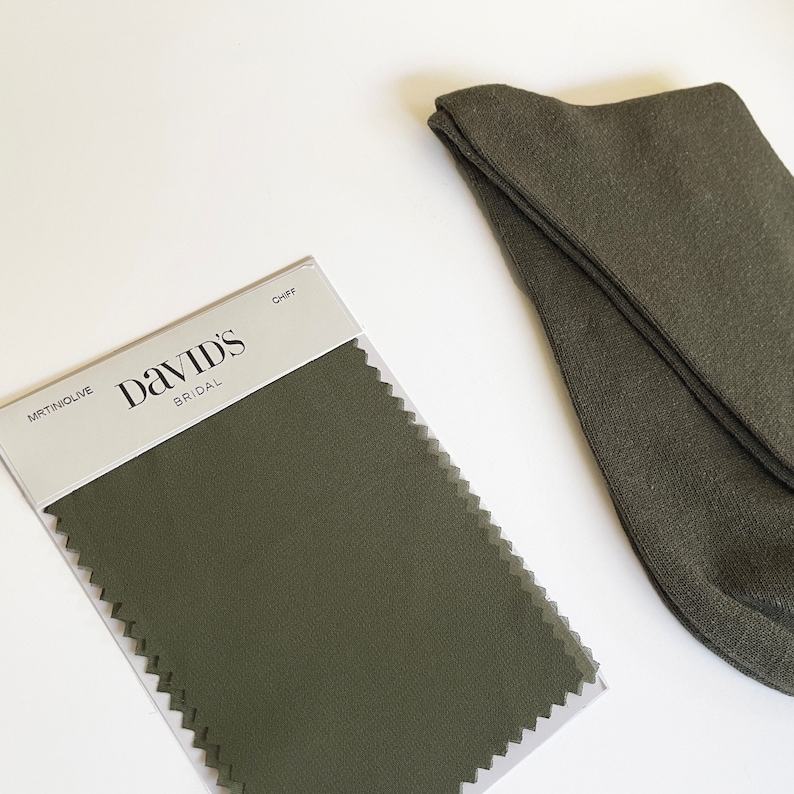May include: An olive green color swatch from David's Bridal next to a pair of olive green socks. The color swatch is labeled "MRTINOLIVE" and "CHIFF". The socks are folded and appear to be made of a soft material.