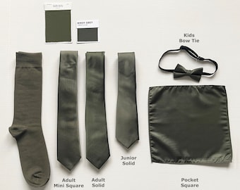 May include: An assortment of olive green formal accessories, including a sock, ties, bow tie, and pocket square. The ties are labelled "Adult Mini Square", "Adult Solid", and "Junior Solid". A "Kids Bow Tie" and "Pocket Square" are also shown. Colour swatches are included.