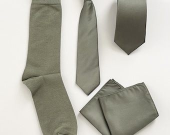 May include: A matching set of olive green accessories, including socks, a clip-on tie, a regular tie, and a pocket square. The items are displayed on a white background, offering a coordinated look.