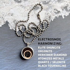 May include: A silver chain necklace with a round pendant made of black, brown, and gold orgonite. The pendant contains shungite, herkimer diamond, atomized metals, quartz, selenite, and black tourmaline. The text "ELECTROSMOG HARMONIZING: ELITE SHUNGITE ORGONITE HERKIMER DIAMOND ATOMIZED METALS QUARTZ / SELENITE BLACK TOURMALINE" is written below the pendant.