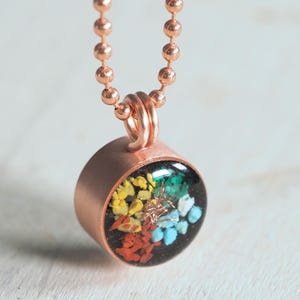 May include: A copper necklace with a round pendant containing pressed flowers and turquoise stones. The pendant is set in a copper bezel.