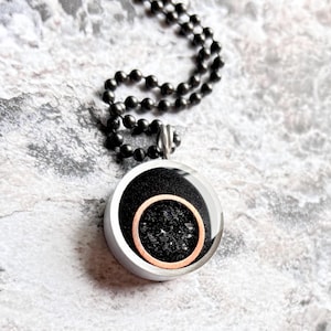 May include: A black and silver necklace with a round pendant. The pendant has a black resin center with a copper ring around it.