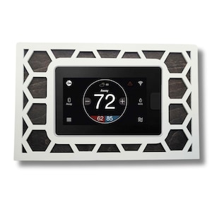 May include: A white thermostat with a black screen displaying a temperature of 72 degrees Fahrenheit. The screen also shows the words "Away" and "62 85". The thermostat is surrounded by a white frame with a hexagonal pattern.