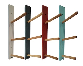 May include: Four wooden towel racks mounted on a wall. The racks are painted in white, black, red, and light blue. Each rack has three wooden dowels for hanging towels.