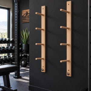 May include: Two vertical light-colored wooden wall racks mounted on a black wall. Each rack features four horizontal cylindrical pegs extending outward and a single small black metal hook positioned at the bottom of each wooden board.