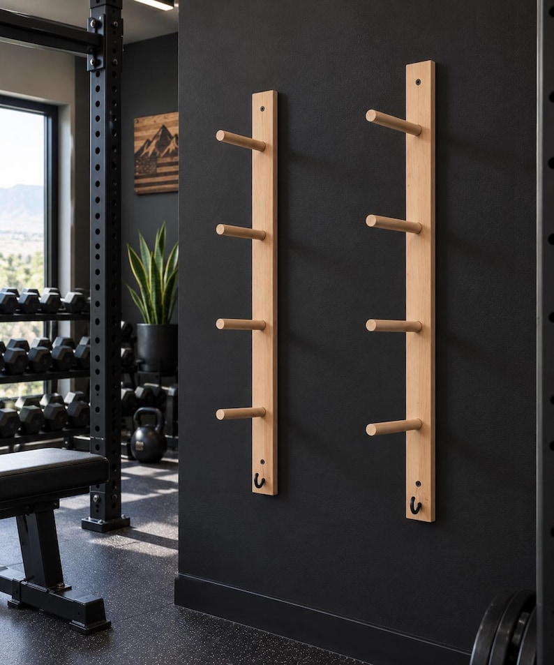 May include: Two vertical light-colored wooden wall racks mounted on a black wall. Each rack features four horizontal cylindrical pegs extending outward and a single small black metal hook positioned at the bottom of each wooden board.