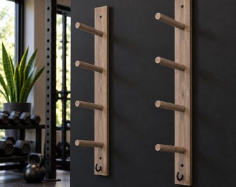 May include: Two vertical light brown wooden wall-mounted racks, each featuring four horizontal cylindrical pegs and a small black metal hook at the bottom, designed for storage and organization of fitness equipment or accessories.