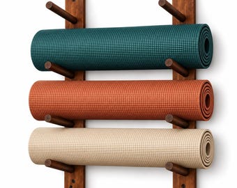 May include: A wall-mounted wooden rack with two vertical supports and six horizontal pegs holding three rolled yoga mats in teal, terracotta, and beige. The rack features two small black metal hooks at the bottom for additional storage.