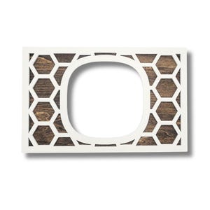 May include: A rectangular white wooden frame with a geometric honeycomb pattern and a central oval opening. The background features a dark wood grain texture, creating a contrast with the white frame.