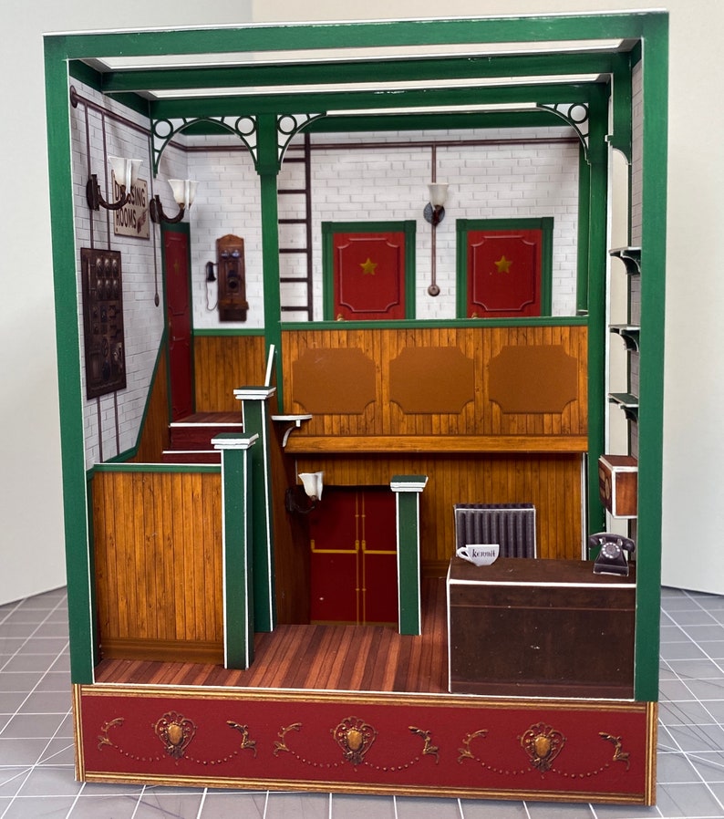 May include: A miniature paper model of a building interior with a wooden counter, a red door, and a sign that reads "Dining Rooms".