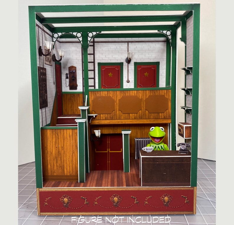 May include: A miniature dollhouse with a green frame, brown wood paneling, and a red brick base. The interior features a wooden counter, a telephone, and a green frog figurine. The dollhouse is decorated with a red and white checkered floor and a red brick base.