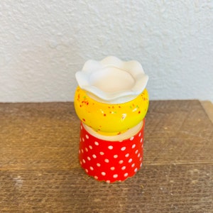 May include: A small, yellow ceramic planter with white polka dots and a white rim. The planter is sitting on top of a red ceramic planter with white polka dots.