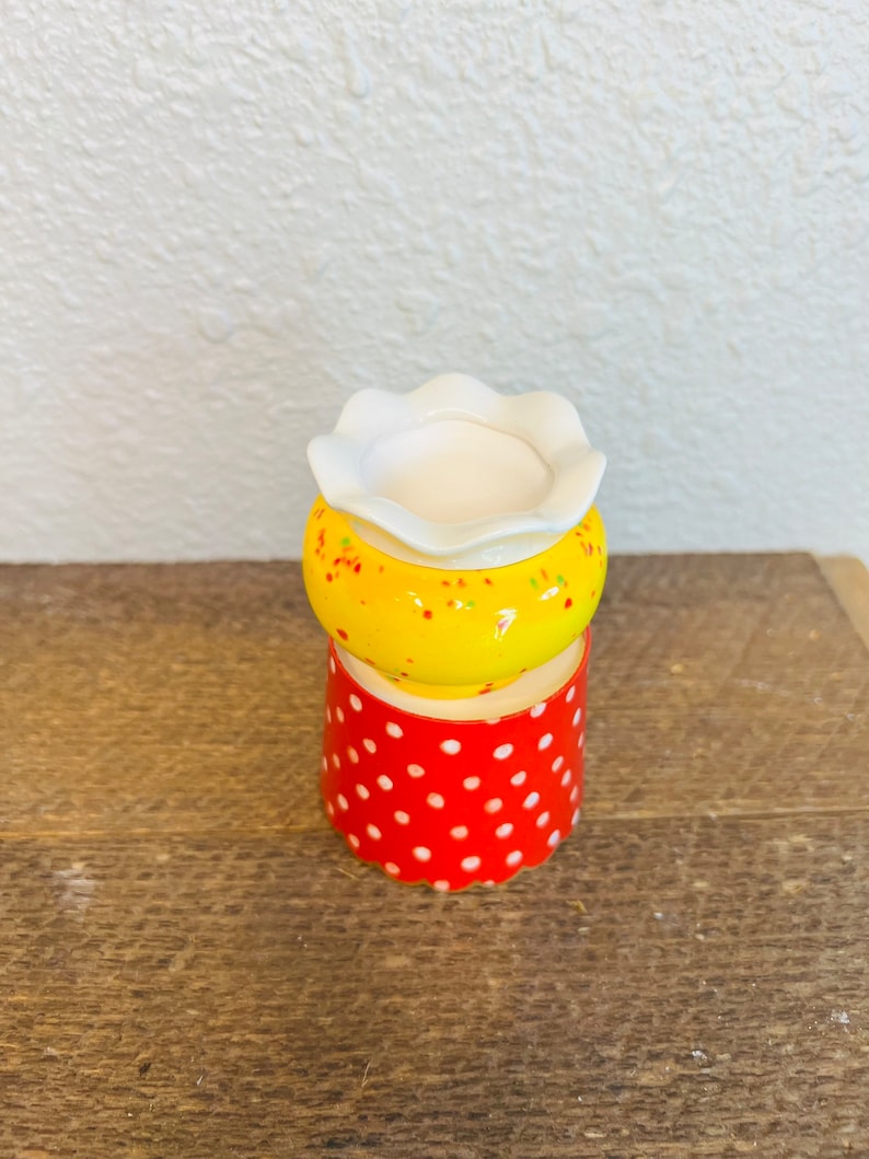 May include: A small, yellow ceramic planter with white polka dots and a white rim. The planter is sitting on top of a red ceramic planter with white polka dots.